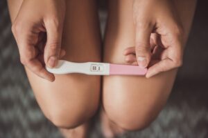woman holding positive pregnancy test on knees